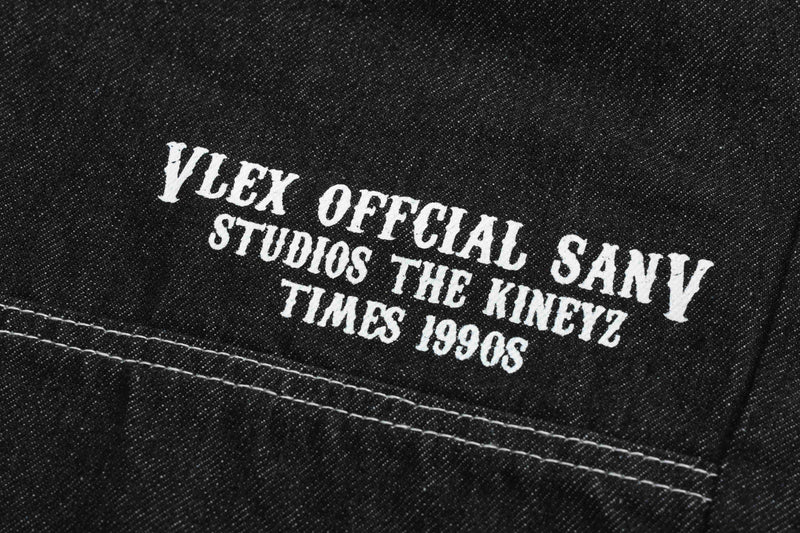 Back leg close-up of black denim shorts with white studio-style text print