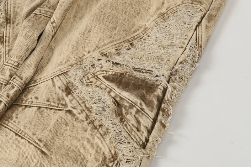 Close-up of beige distressed jeans with frayed side panel and torn knee detail