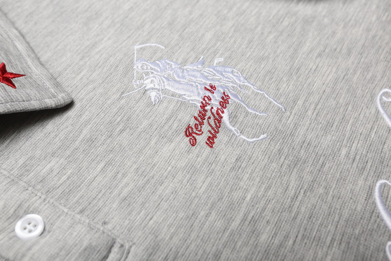 Close-up of a light gray embroidered gothic polo shirt with white and red stitched lettering and cotton texture