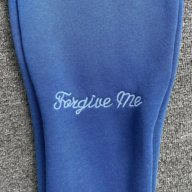 The Syna World Blue Letter Print Drawstring Jogger Pants feature blue fabric with “Forgive Me” embroidered in light blue cursive, making them perfect for stylish streetwear or cozy loungewear.