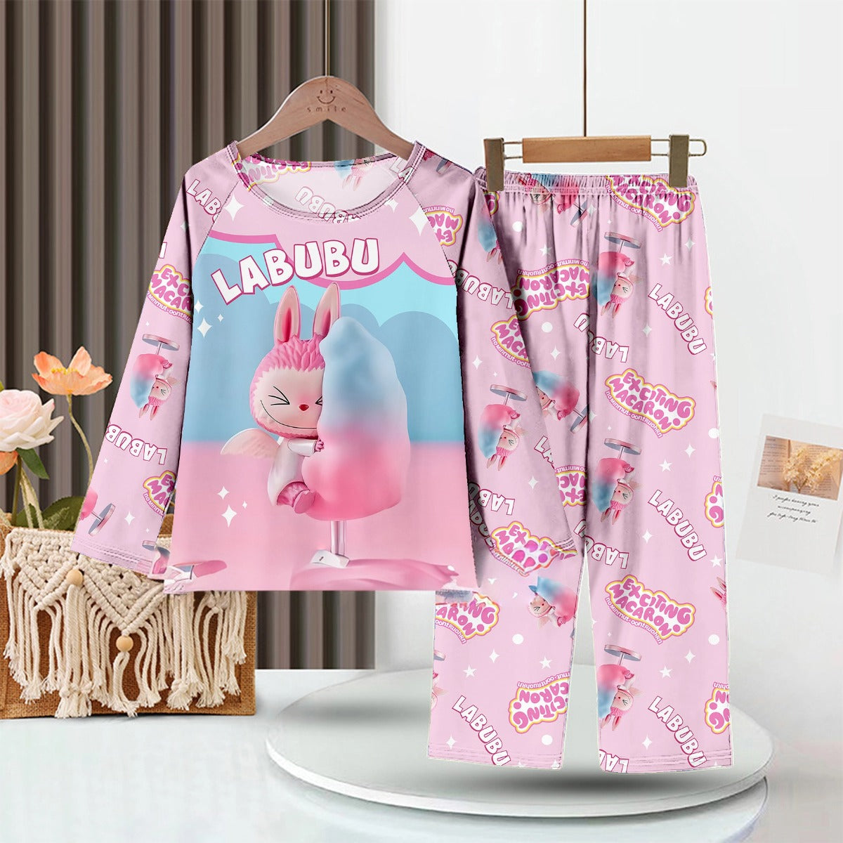 The LABUBU Baby Pajama Set - &quot;Exciting Macaron&quot; features a pink milk silk fabric adorned with playful patterns. It depicts a cartoon character with a cotton candy-like object, capturing childhood whimsy in its long-sleeve top and pants.