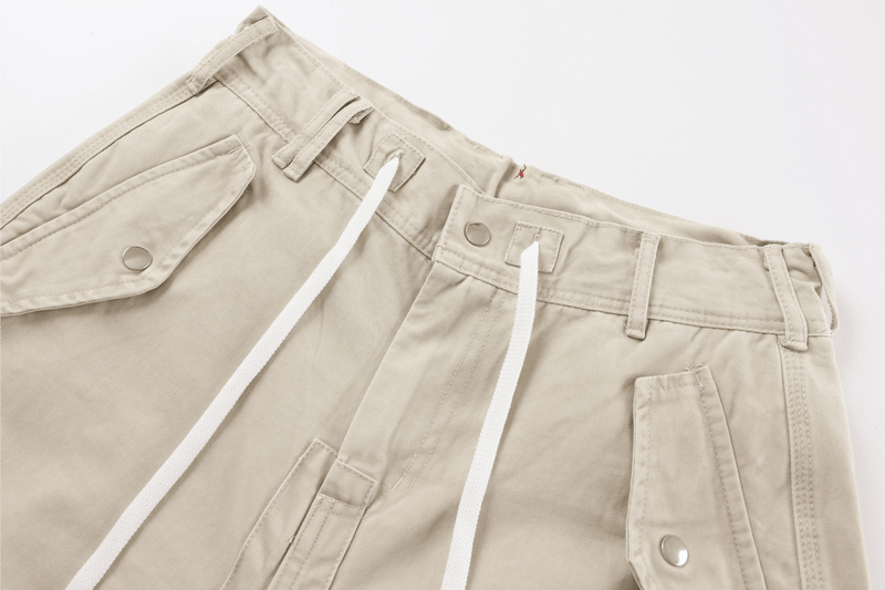 Close-up of beige cargo pants waistband with white drawstrings and snap-button flap pockets