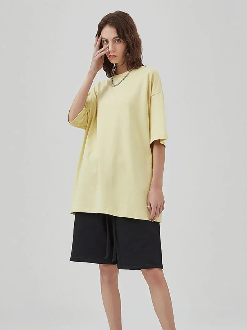 A person poses against a plain background in the Custom Anime Character Butter Yellow T-Shirt— a personalized 230GSM 100% cotton tee — paired with black knee-length shorts and a chain necklace, one hand partly covering their face.