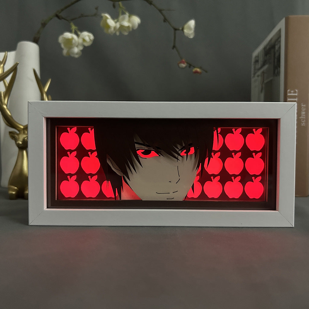 The Death Note Anime Light Box – Light Yagami 3D LED Lamp by Death Note features a dark-haired anime character with red apples, echoing Light Yagami. It is illuminated from behind with dynamic color-changing effects, and includes decorative objects and a book in the blurred background.