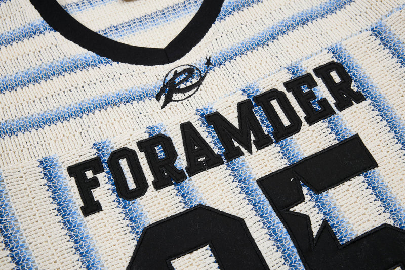 Close-up of a cream knit tee with blue varsity stripes, black ribbed collar, and bold embroidered FORAMODER lettering