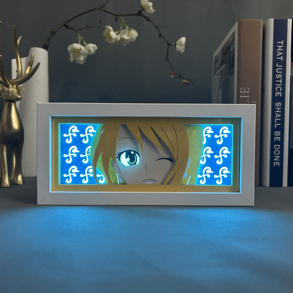 The Seakoff Nami One Piece 3D Anime Light Box features a winking anime face amid glowing blue music notes. It includes a gold deer figurine and book stack, while an elegant branch with white flowers enhances the ambiance. Features LED lamp with 16 colors and remote control.