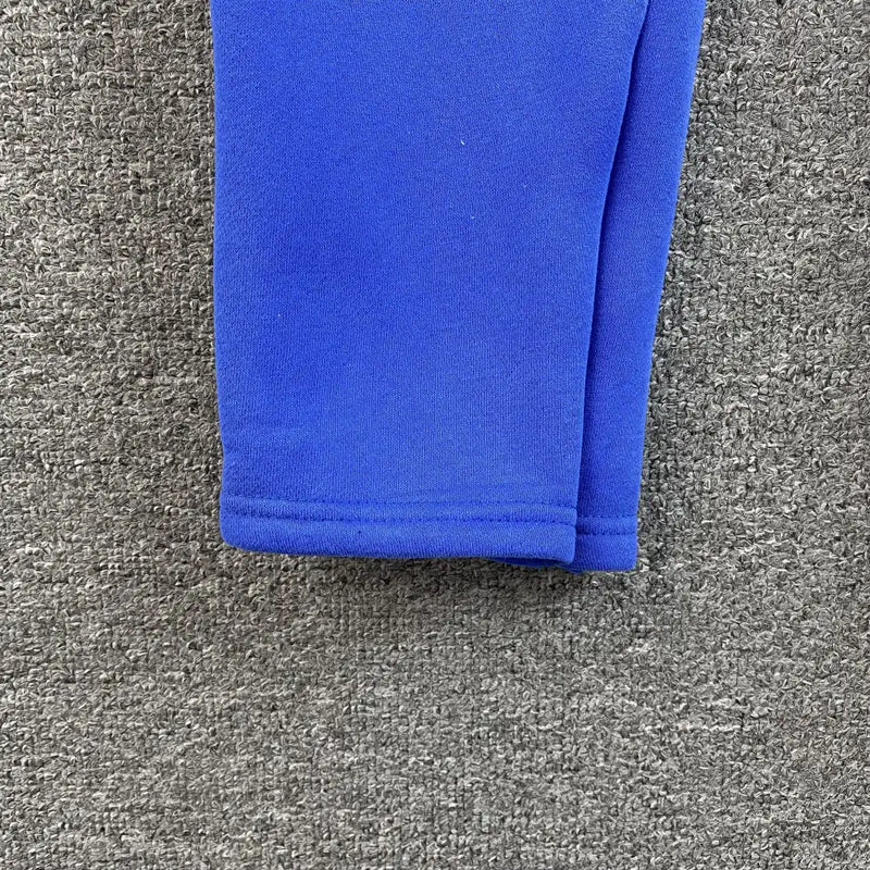A close-up of the bottom hem of Syna World Blue Graffiti Graphic Jogger Pants on a gray textured carpet.