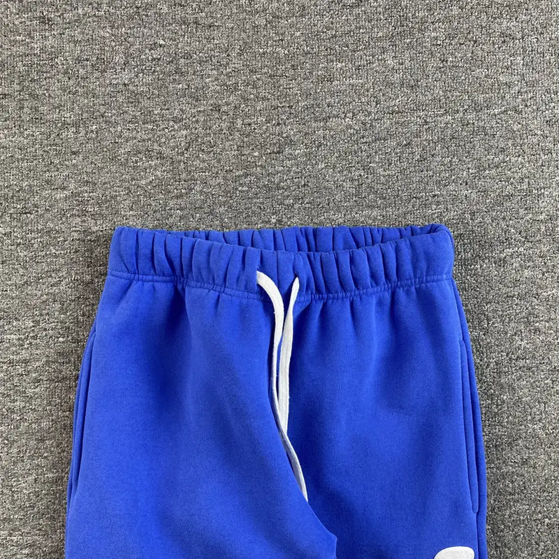 The Syna World Blue Graffiti Graphic Jogger Pants, featuring a white drawstring, are laid flat on a textured gray surface—ideal for adding bold color to your streetwear collection.