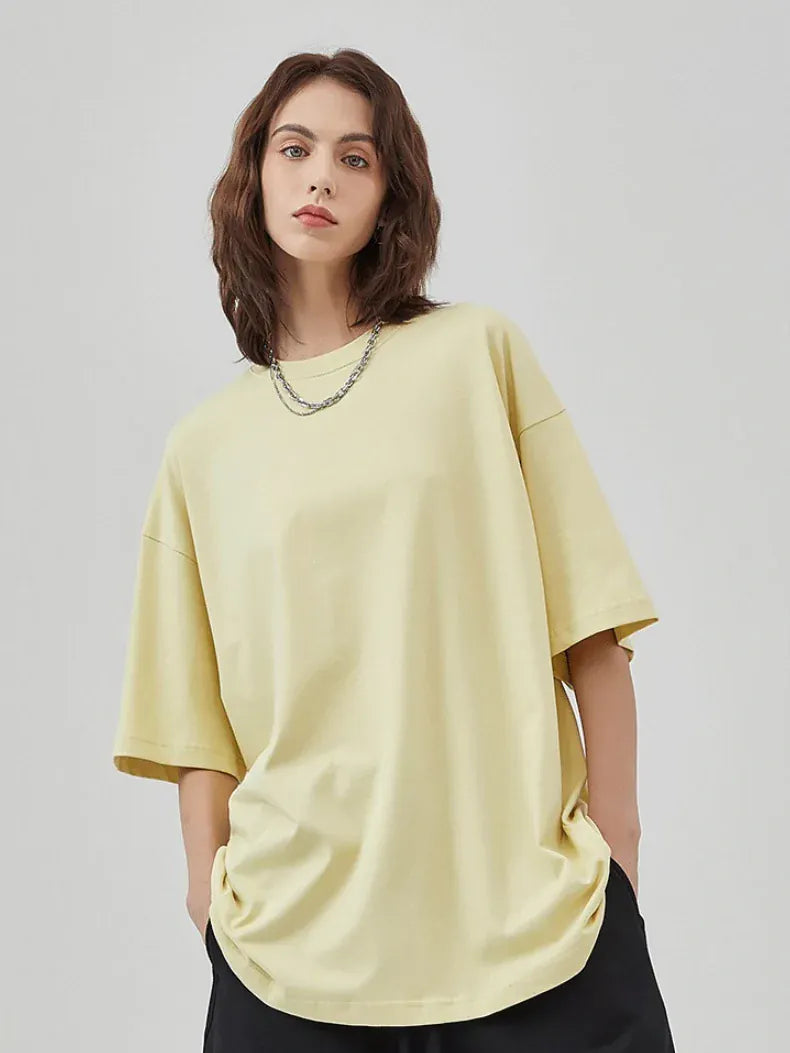 A person with shoulder-length brown hair wears the Custom Anime Character Butter Yellow T-Shirt—Personalized 230GSM 100% Cotton Tee—with a chain necklace and black pants, standing against a plain light gray background.