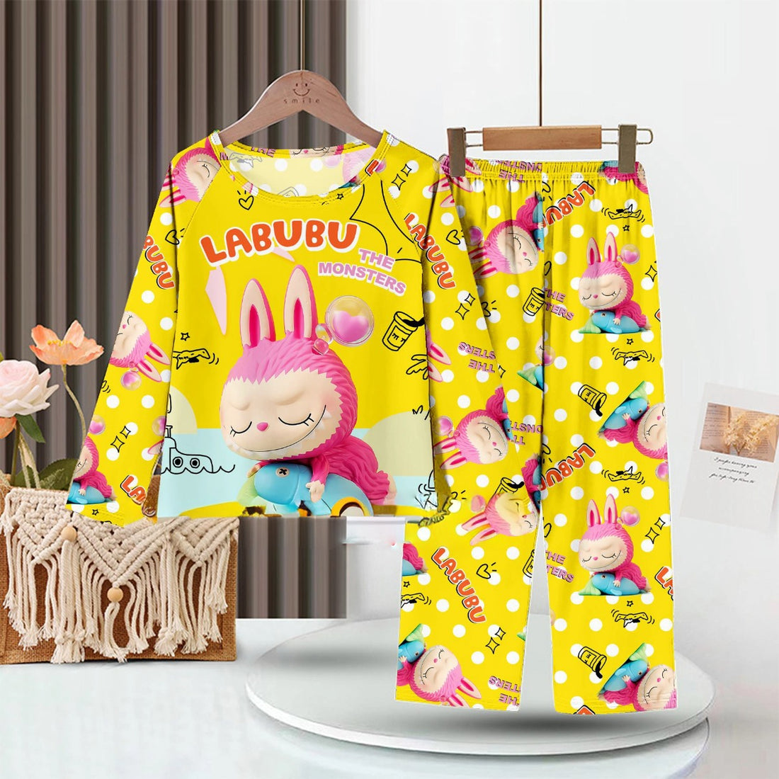 The LABUBU Baby Pajama Set, featuring &quot;The Monsters&quot; theme, is a bright yellow sleepwear crafted from premium milk silk fabric. It showcases colorful cartoon characters, including a pink and blue long-eared creature. It&