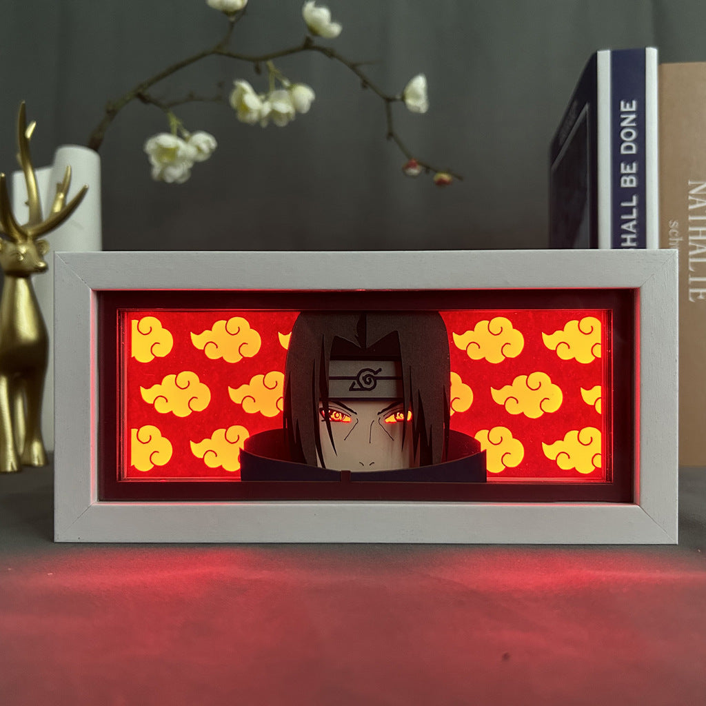 The Naruto Anime Light Box features Itachi Uchiha with glowing red Mangekyou Sharingan-like eyes and headband, set against a backdrop of red clouds. Complemented by a metallic deer and books, it offers a 3D effect with 16-color adjustable LED lights.