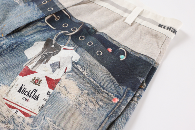 Front pocket area of faded patchwork jeans with hanging tag and printed belt detail