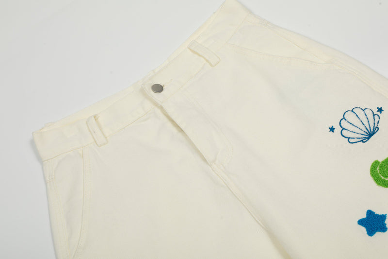 Close-up of cream cargo pants waistband with snap button and embroidered shell detail