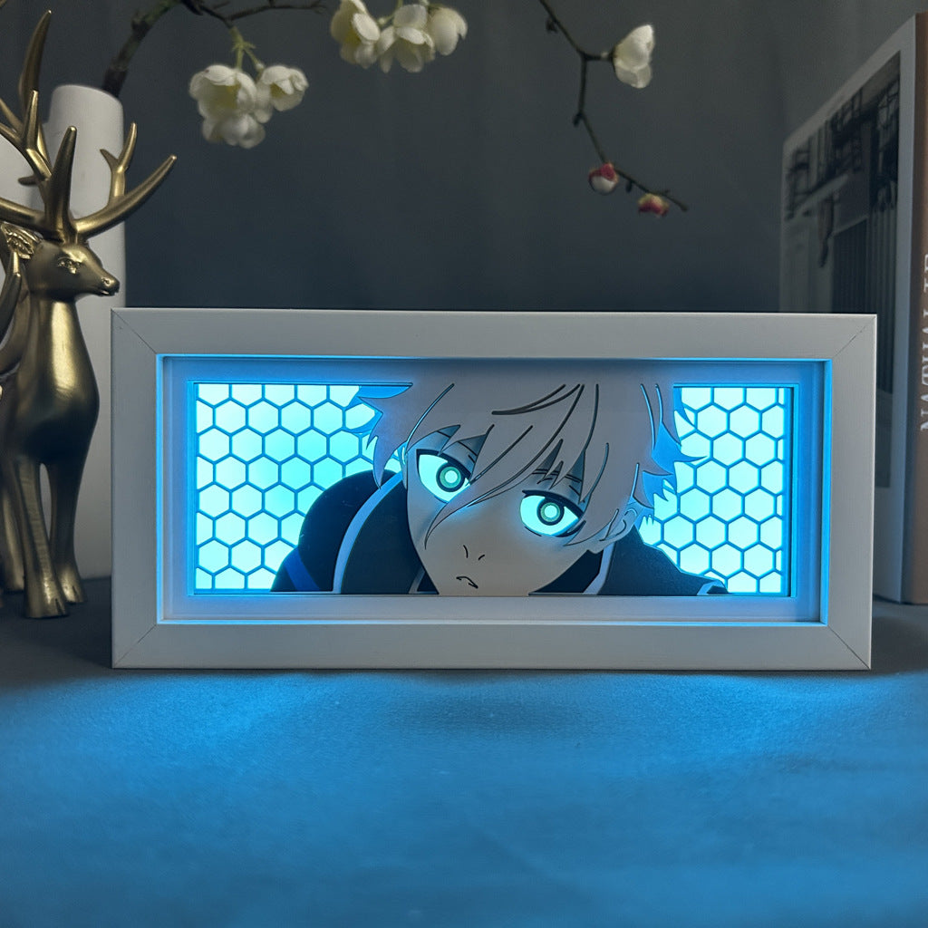 The "Toshiro Hitsugaya Bleach 3D LED Light Box – Anime Lamp with 16 Color Modes" by Bleach features a framed image of Toshiro Hitsugaya with white hair and blue eyes, set against a blue honeycomb-patterned background. Nearby is a decorative brass deer and floral branch.