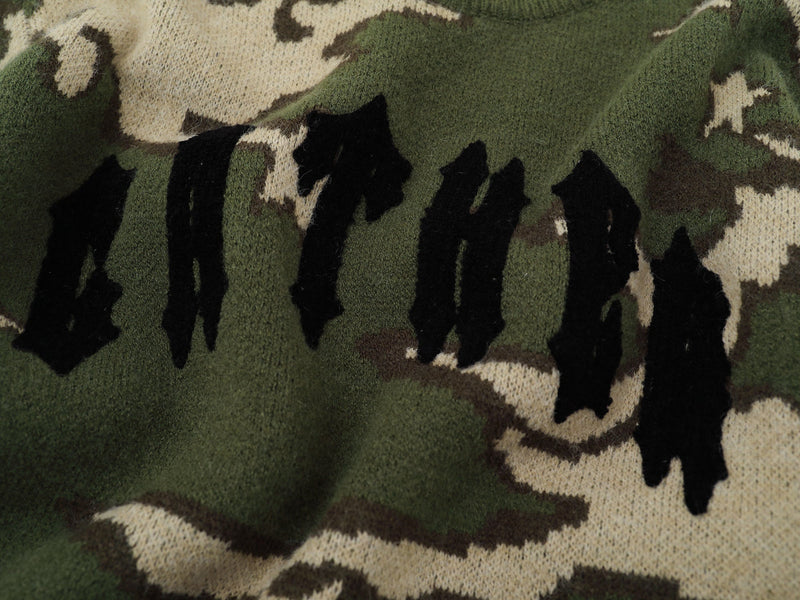 Close-up of black gothic logo knit on green camouflage sweater front