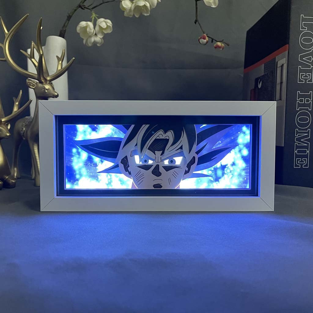 The Seakoff Ultra Instinct Goku 3D LED Light Box, inspired by Dragon Ball Super, showcases an anime character in a dynamic pose with blue light. It complements table decor like a metallic deer figurine and &quot;Love Home&quot; book, adding charm to the setup.