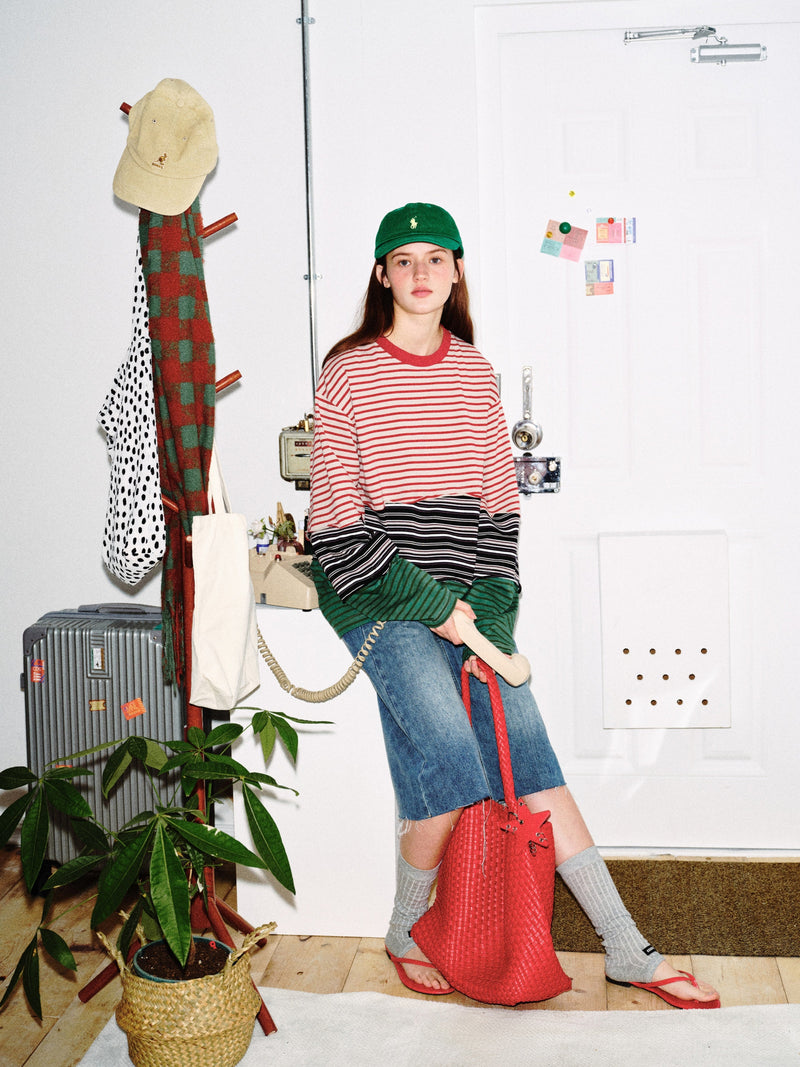 Model seated in color-block striped long sleeve tee with red, black, and green striped blocks