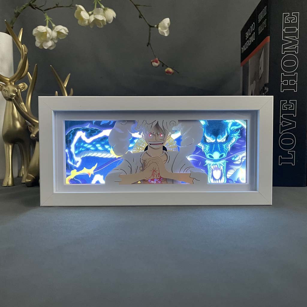 The Seakoff Gear 5 Luffy vs Kaido 3D LED Light Box showcases an animated scene with dynamic blue and white energy, ideal for One Piece fans. It is displayed with a gold deer figurine, the book &quot;LOVE HOME,&quot; and orchids above.