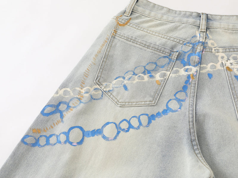 Close-up of back pocket and waistband on light wash denim pants with painted chain design