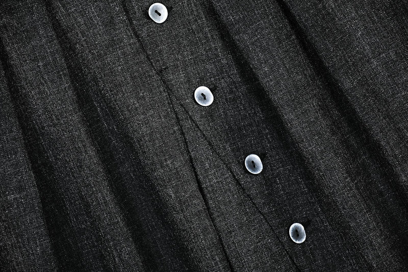 Close-up of black textured fabric with front buttons and pleat seams