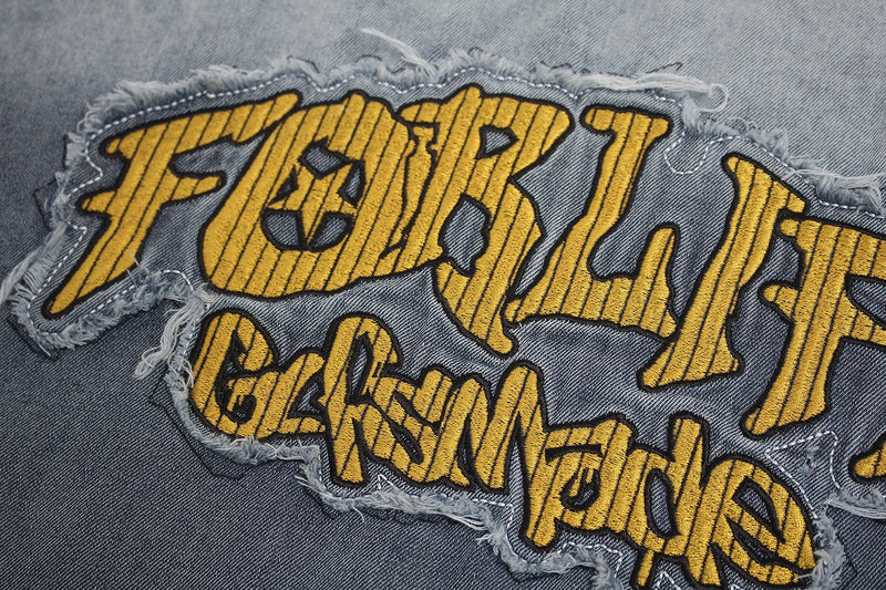 Close-up of distressed yellow embroidered Feral Peace graphic on faded denim-style fabric