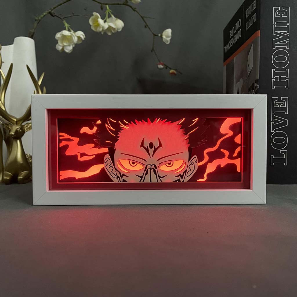 The Sukuna LED 3D Light Box – Jujutsu Kaisen Cursed Energy Glow features an anime character with intense eyes and spiky hair, engulfed in red flames. A white frame contrasts the decor, with &quot;LOVE&quot; on the side. Ideal for fans and collectors of Jujutsu Kaisen seeking a striking piece.