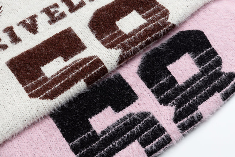 Close-up of brown varsity lettering on white fuzzy knit sweater with pink sweater underneath