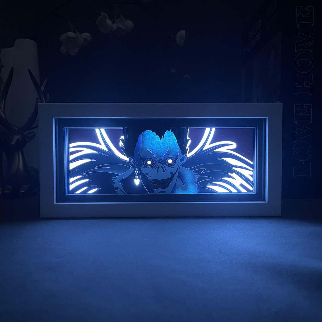 The Ryuk LED 3D Light Box – Death Note Shinigami Glow Decor by Death Note features a rectangular display with a stylized image of a blue-headed character with large eyes and wings on a dark backdrop. Perfect for anime fans, it&