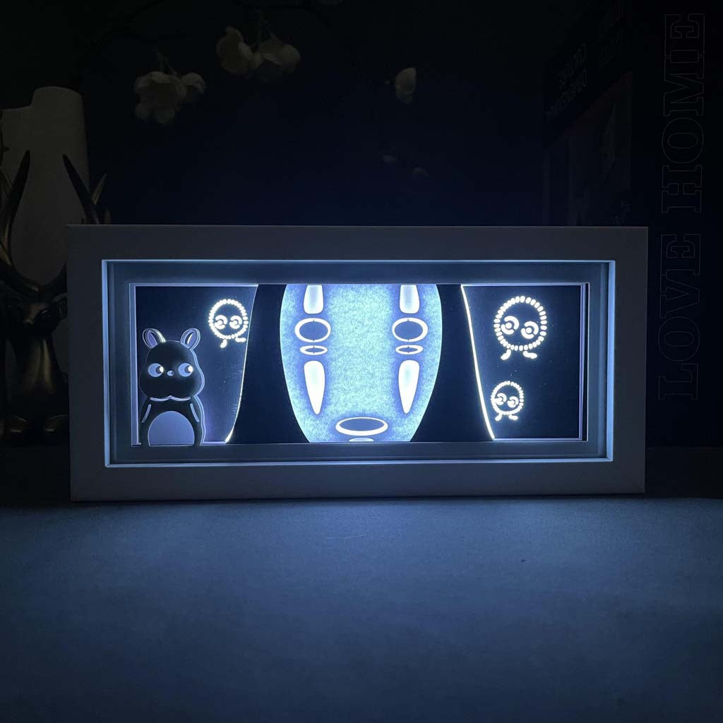 The Spirited Away Studio Ghibli LED 3D Light Box features silhouettes of Totoro, No-Face, and Soot Sprites against a luminous backdrop. Framed in white, this elegant decor is ideal for any anime fan&