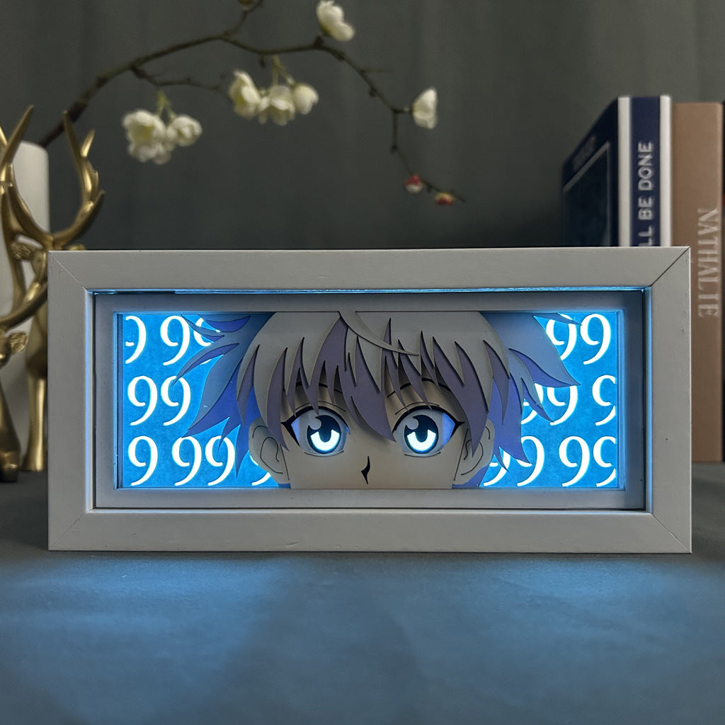 The Hunter x Hunter Killua Zoldyck Anime Light Box features his eyes and hair against a blue background with the number 99, backlit by 16-color adjustable LED lighting. Books and a decorative object with branches complete the scene in the background.