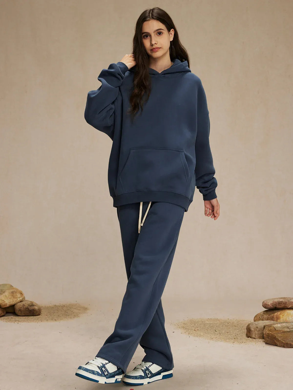 A person stands indoors wearing a Custom Anime Character Navy Hoodie - Personalized 350GSM 100% Cotton Pullover and matching sweatpants, with blue-and-white sneakers and rocks arranged on the floor.