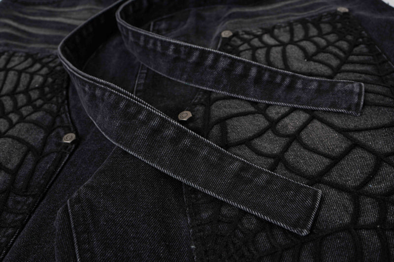 Close-up of black denim shorts with overlapping straps across spiderweb panels