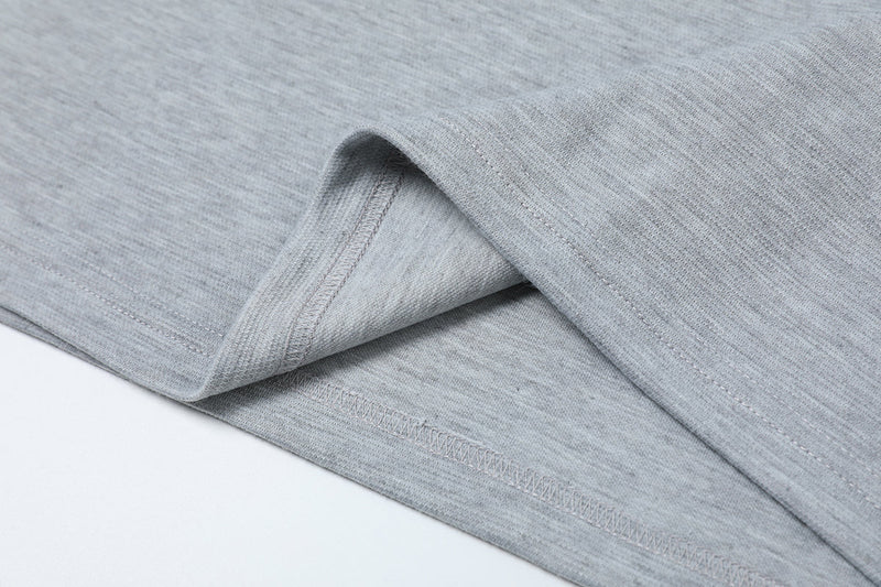 Close-up of a light gray oversized tee hem with asymmetric seam stitching and folded streetwear fabric detail