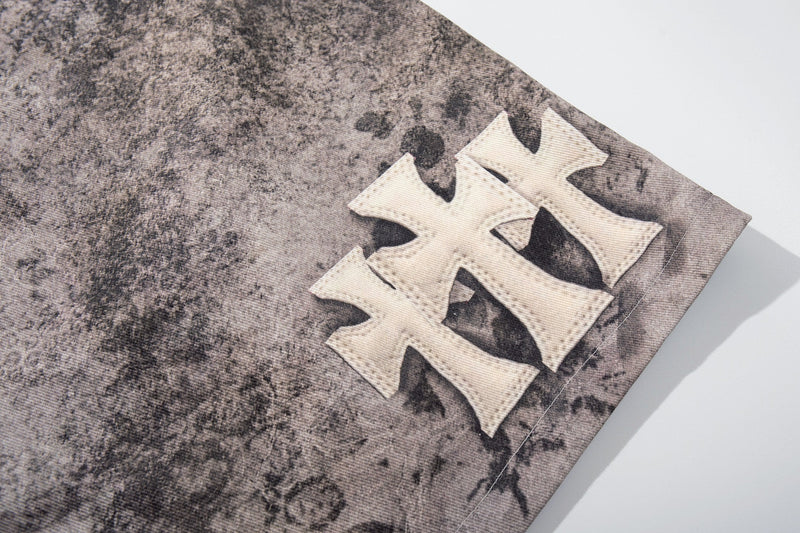 Close-up of white cross patch on washed gray denim shorts at the leg opening