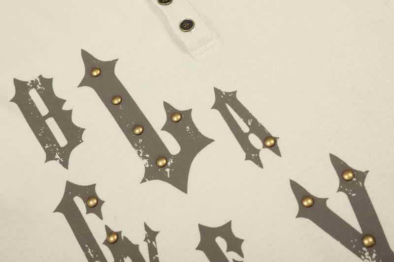 Cream tee front graphic close-up with gothic lettering and gold-tone studs