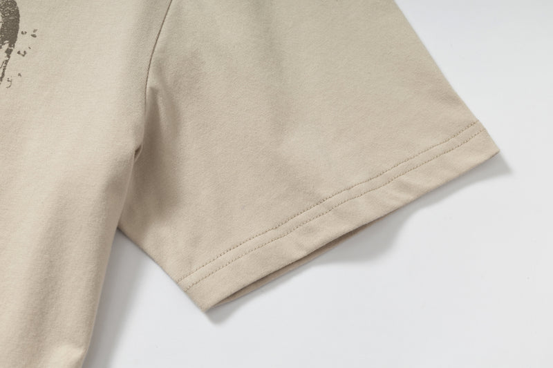 Beige layered graphic tee sleeve with double-stitched hem and subtle streetwear print detail