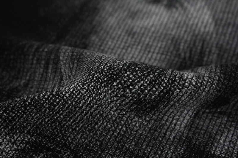 Close-up of black textured graphic tee fabric with subtle shadow portrait print and studded mock-neck detail