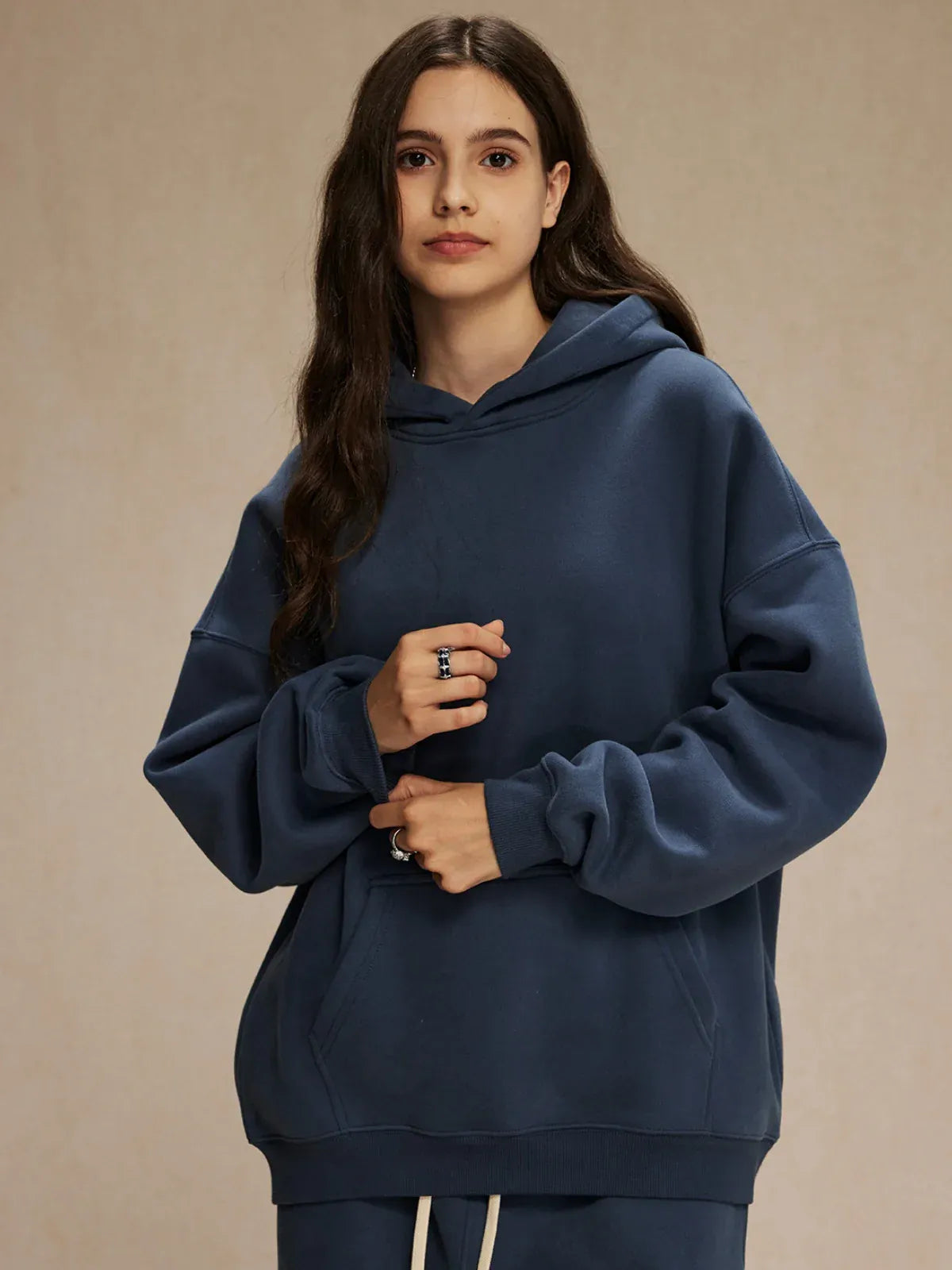 A person with long brown hair is standing against a plain beige background, wearing a loose-fitting Custom Anime Character Navy Hoodie—Personalized 350GSM 100% Cotton Pullover—and matching pants.