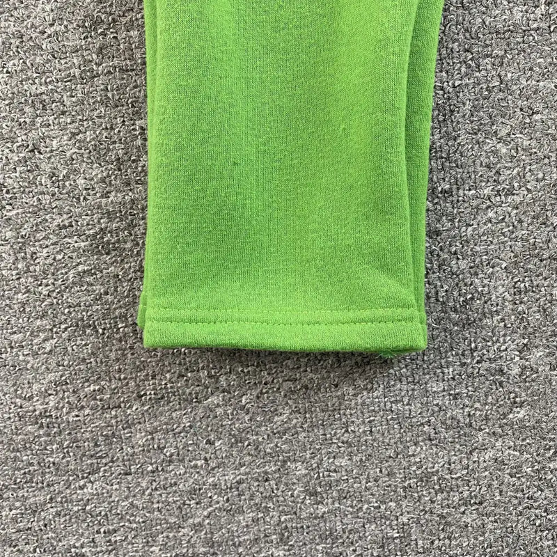 A close-up of the Syna World Green Yellow Letter Print Drawstring Jogger Pants hem, set against a textured gray carpet—ideal for injecting streetwear flair into your look.