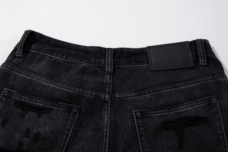 Close-up of back waistband on deep charcoal jeans with black logo patch and belt loops