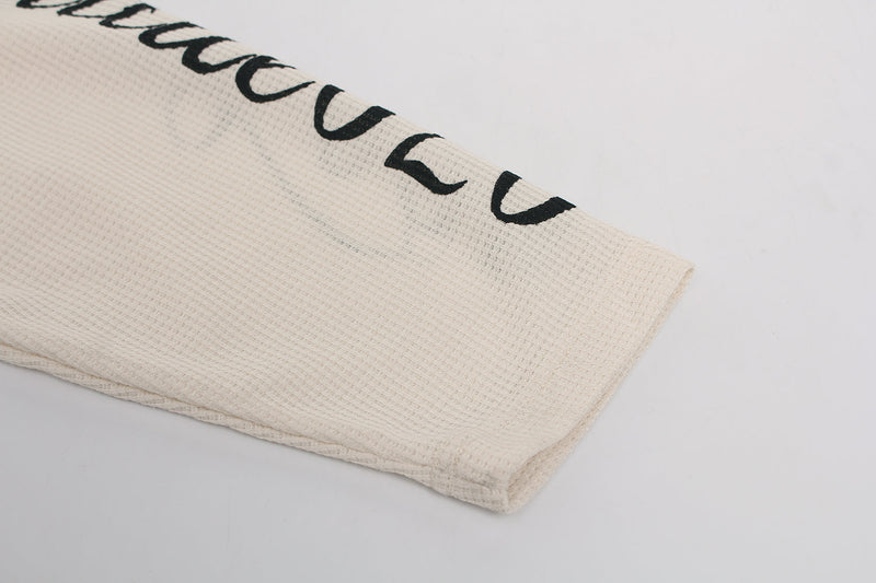 Close-up of cream waffle knit sleeve hem with black printed script along the cuff