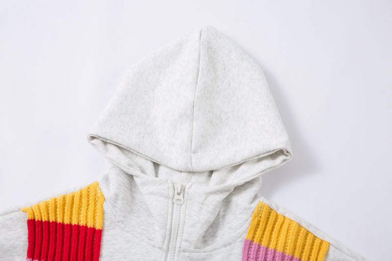 Close-up of the hood and upper front zipper on a light gray hoodie with colorful knitted scarf panels