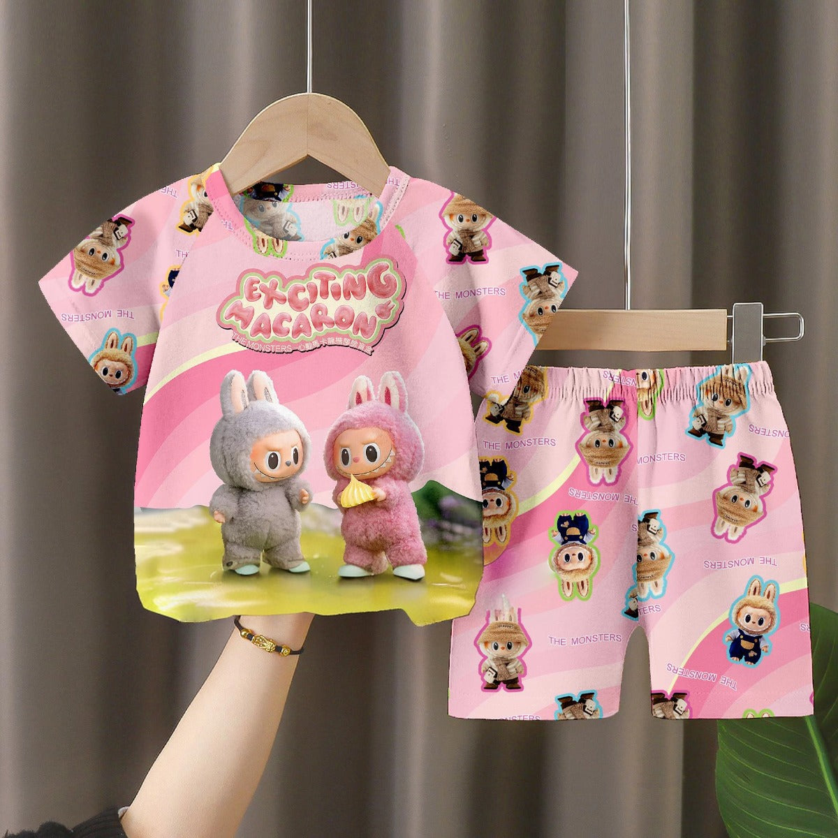 The LABUBU &quot;Exciting Macaron&quot; Baby Pajama Set in soft milk silk features a fun cartoon design with characters in animal costumes. This pink sleepwear, adorned with &quot;Exciting Vacation&quot; text, promises sweet dreams for little ones.