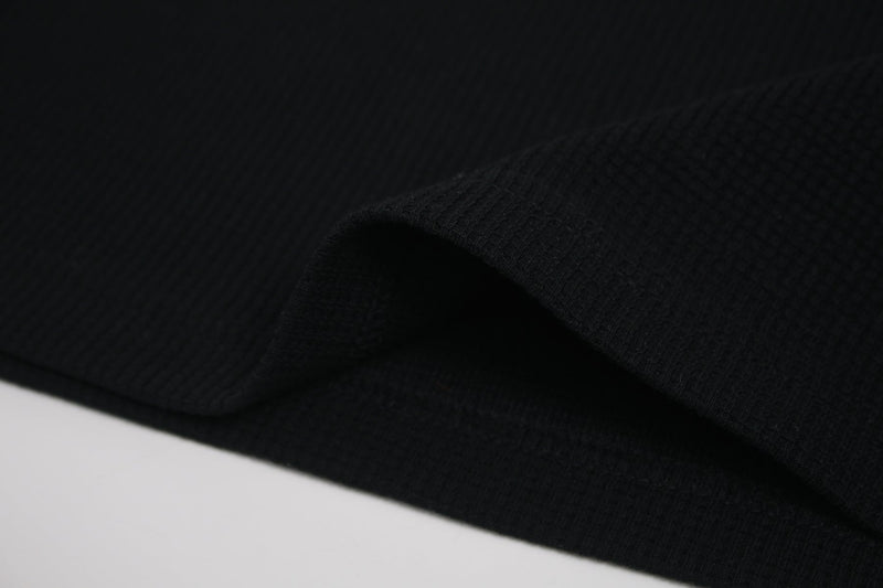Black ribbed short sleeve tee fabric with a close-up folded hem and subtle texture on a minimalist background