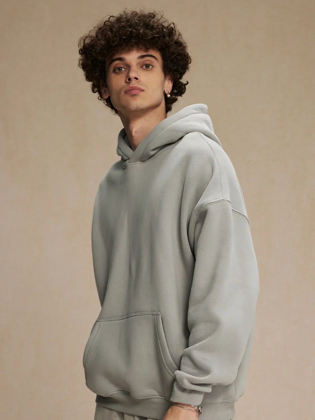 A person with curly hair is wearing the Custom Anime Character Light Gray Hoodie – a personalized 350GSM 100% cotton pullover – while standing against a plain beige background.