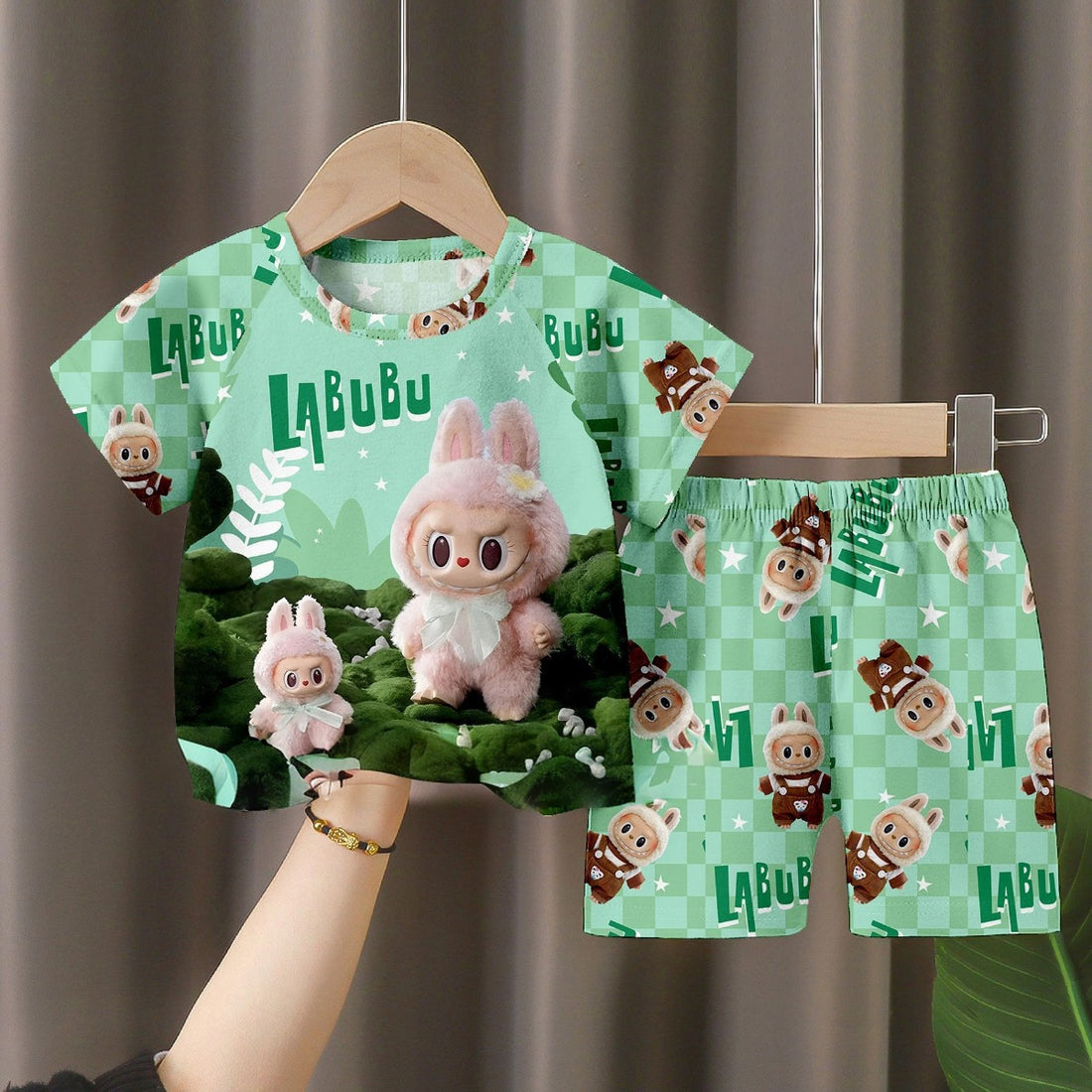 The LABUBU Baby Pajama Set features a cozy green short-sleeve shirt and matching shorts made from soft milk silk. The bunny-themed design showcases cartoon rabbits on a lively background with &quot;LABUBU&quot; printed on the shirt.