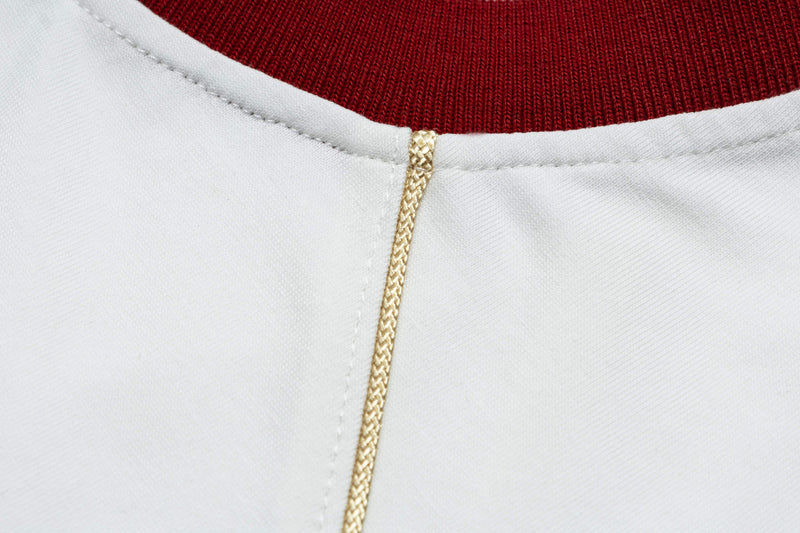 Close-up of a retro football jersey tee with burgundy knit collar, white fabric, and gold braided trim