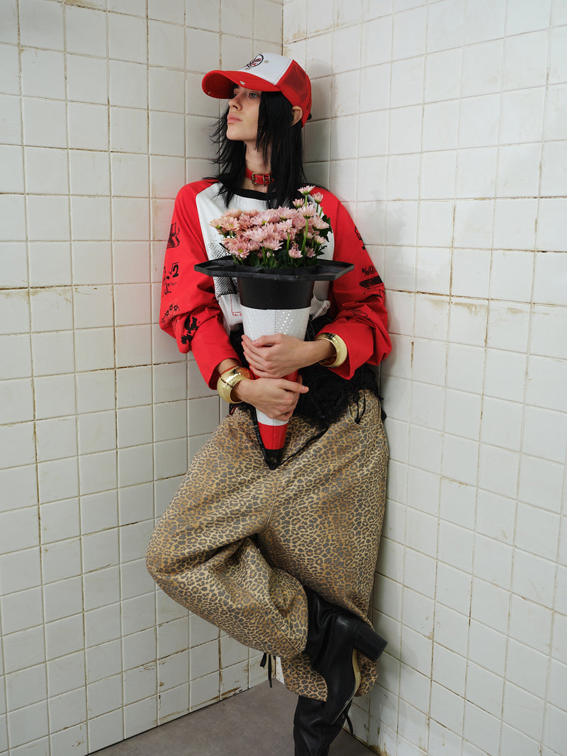 Model leaning in corner wearing red and white graphic raglan long-sleeve T-shirt and holding flowers