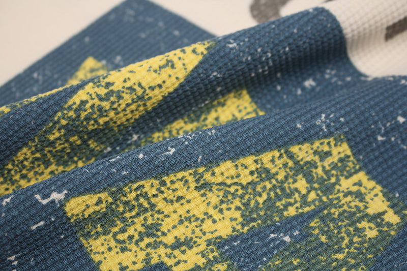 Close-up of a blue waffle knit streetwear tee with yellow graphic print and textured fabric detail