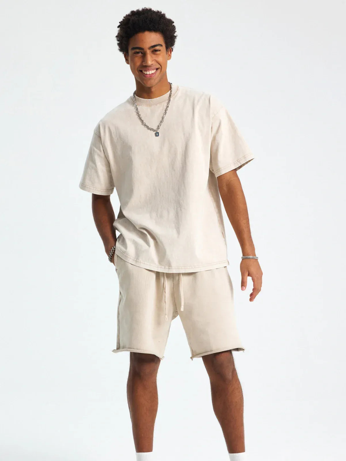 A man smiles in a Custom Anime Character Beige Washed T-Shirt - Personalized Anime Style Tee and matching shorts, accessorized with a silver necklace and bracelet, against a plain light background.